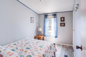 Un dormitorio con cama, mesita de noche, lámpara, ventana con cortinas y adornos en la pared.