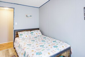 A bedroom with a bed, a wooden headboard, a single wall with a small picture, and a door.