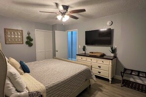 Ein Schlafzimmer mit einem Bett, einer Kommode, einem Deckenventilator und einem Fernseher an der Wand.