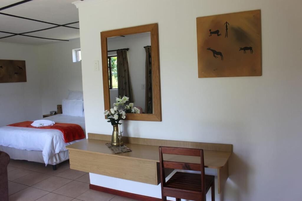 Habitación de hotel con cama, escritorio de madera, silla, espejo y obras de arte en la pared.