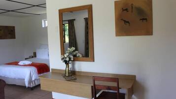 Habitación de hotel con cama, escritorio de madera, silla, espejo y obras de arte en la pared.