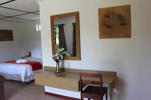 A hotel room with a bed, a wooden desk, a chair, a mirror, and artwork on the wall. - Thornycroft Lodge & Spa KuGompo (KuGompo City)