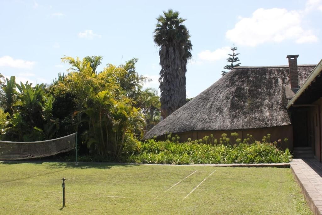 Un bâtiment à toit de chaume, doté d’une pelouse bien entretenue et d’une végétation tropicale.