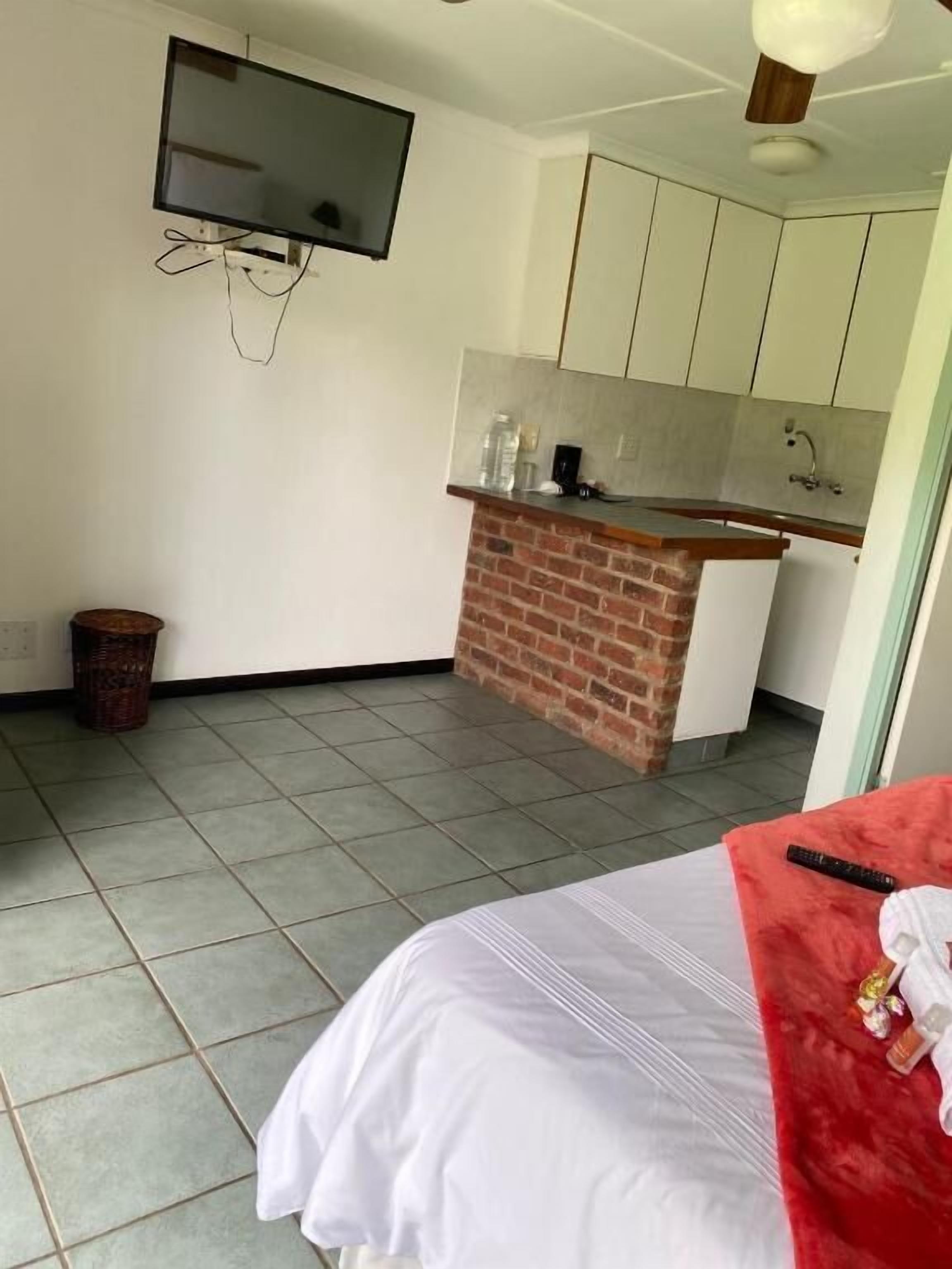 Una camera d'albergo con un letto, una TV a parete, un angolo cottura con un bancone in mattoni e un pavimento piastrellato.