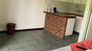 Une chambre d’hôtel comprenant un lit, un téléviseur fixé au mur, un petit coin cuisine avec un comptoir en briques et un sol carrelé.