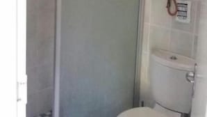 Un bany amb vàter, plat de dutxa i un calefactor penjat a la paret.
