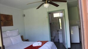 Une chambre d’hôtel comprenant un lit, un ventilateur de plafond, une salle de bain avec des toilettes et un lavabo, ainsi qu’une kitchenette équipée d’un réfrigérateur.