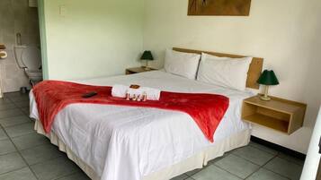 Une chambre avec un lit simple, une tête de lit en bois, du linge de lit blanc, un plaid rouge, des lampes de chevet et un tableau au mur.