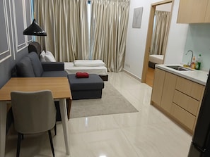 Ein moderner Wohnraum mit Sofa, Hocker, Esstisch und einer Küchenzeile mit Spüle.