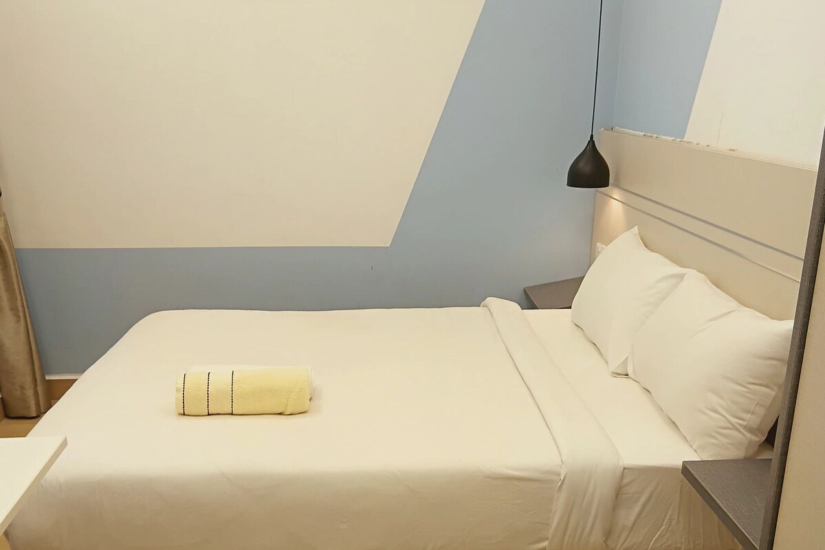 Ein ordentlich bezogenes Bett mit weißer Decke und Kissen, ein Nachttisch mit Lampe sowie eine Wand mit drei gerahmten Bildern.