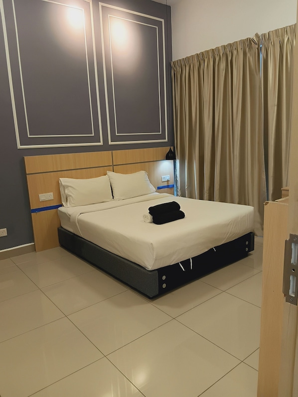 Una cama bien hecha con colchón y almohadas blancos, cabecera de madera, mesita de noche con lámpara y cortina en la ventana.