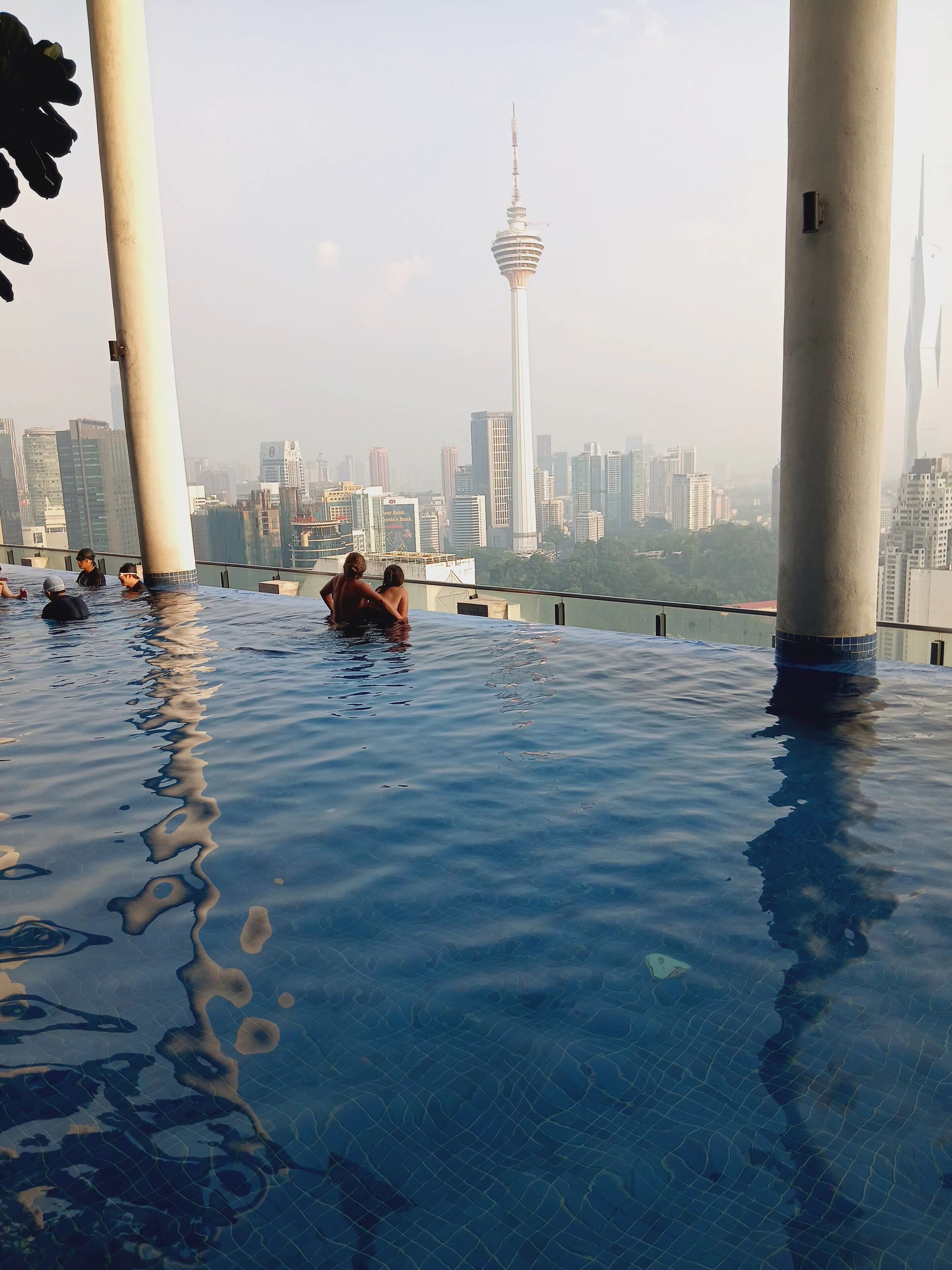 Piscina infinita con vista al horizonte urbano, incluyendo una torre destacada.