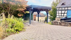 A paved pathway leading to a covered structure with a view of residential buildings and a car parked nearby.