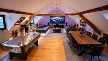 A cozy living room with a pool table, a dining table, and a large flat-screen TV mounted on the wall.