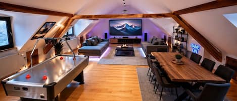 A cozy living room with a pool table, a dining table, and a large flat-screen TV mounted on the wall.