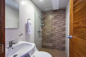Een moderne badkamer met een douchecabine van glas, een wit wastafelmeubel en een houten deur.