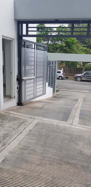 Une entrée fermée par un portail en métal donnant accès à un immeuble, avec un chemin en béton menant à un espace de stationnement.