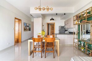 Een moderne keuken met roestvrijstalen apparatuur, een eethoek met houten stoelen en een glazen tafel, en een decoratieve lamp erboven.