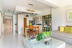 Ein modernes Wohnzimmer mit einem Glastisch, ein Essbereich mit Holzstühlen, eine Küche mit integriertem Regal und eine Treppe zu einer weiteren Ebene.