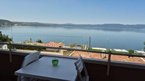 Un balcón con mesa y sillas, con vistas a un lago tranquilo y colinas a lo lejos.