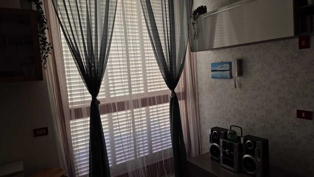 A room with a window covered by sheer curtains, a wall-mounted speaker system, and a small framed picture. - The Oasy in the Lake (Lazio)