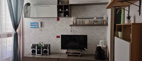 A living room with a flat-screen TV, two speakers, a bookshelf, and a small table with a lamp.