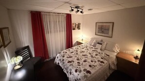 Une chambre d’hôtel avec un lit, des lampes de chevet, une table avec une lampe, une chaise et une fenêtre avec des rideaux.