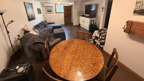 Un salon avec une table ronde en bois, un canapé, un téléviseur et une croix accrochée au mur.