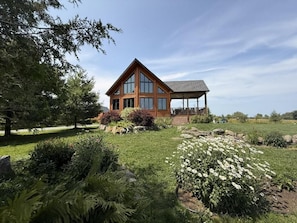 A wooden house with a large porch and a covered area, surrounded by a well-maintained garden with various plants and a lawn. - Orford - L'Indien qui dort, private suite with breakfast included (Eastman)