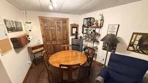 Un coin repas avec une table et des chaises en bois, un fauteuil bleu et une bibliothèque contenant divers objets.
