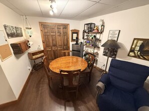 A dining area with a wooden table and chairs, a blue armchair, and a bookshelf with various items. - Orford - L'Indien qui dort, private suite with breakfast included (Eastman)