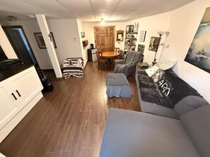Een woonkamer met een bank, een eettafel met stoelen en een keuken met kasten.
