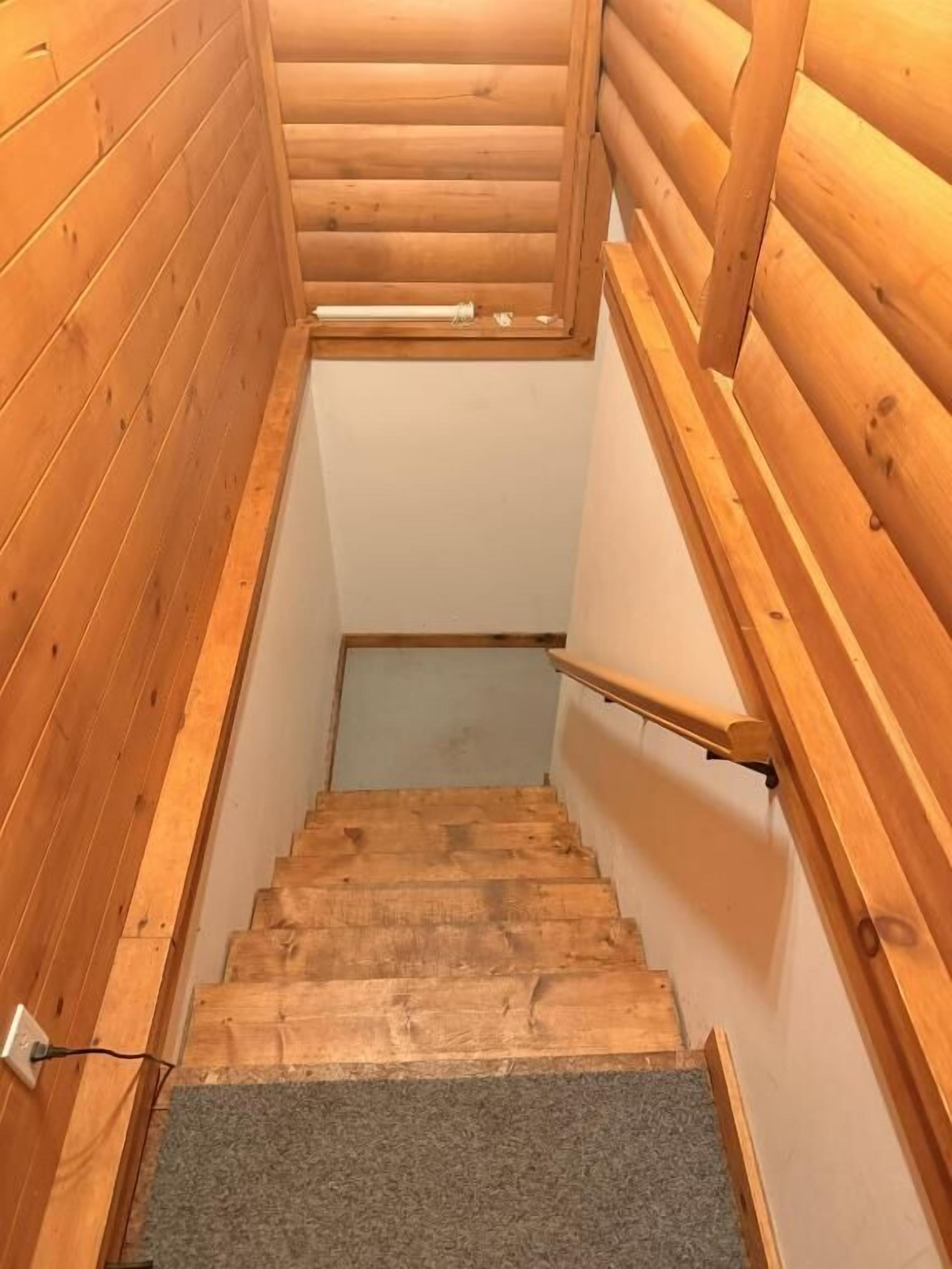 Un escalier en bois avec une rampe, des marches recouvertes de moquette et une fenêtre en haut.