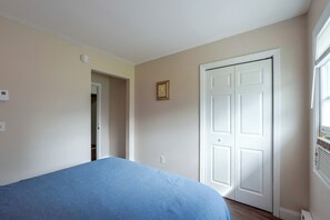 A bedroom with a single bed, a door, a small picture frame, and a thermostat on the wall.