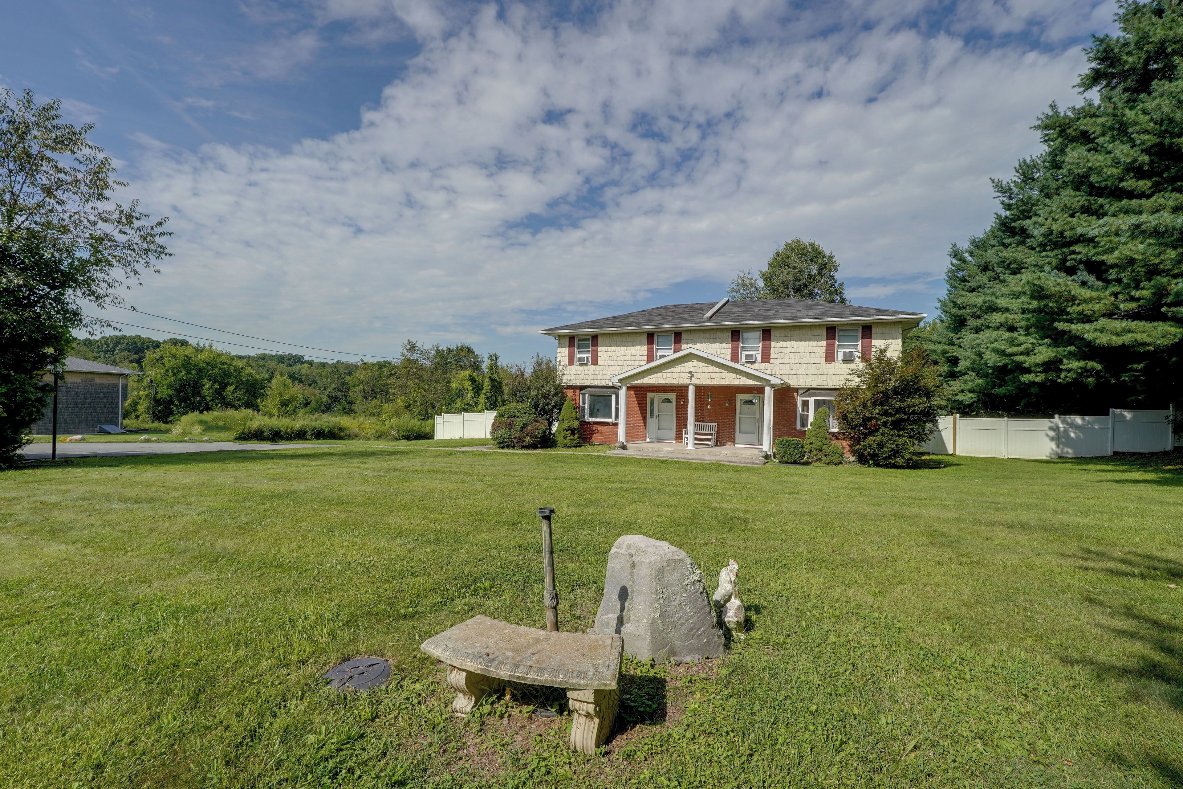 A two-story house with a front porch, a lawn, and a stone bench.