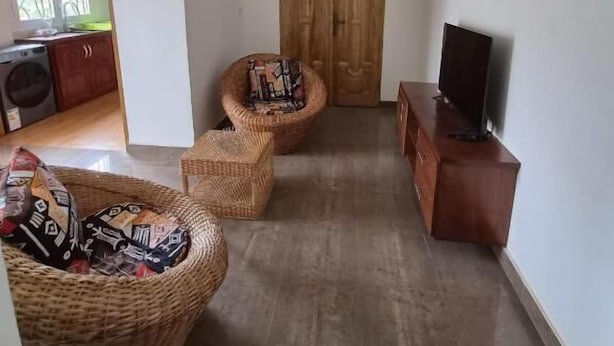 Een woonkamer met een televisie op een houten kast, een rieten bank en een rieten stoel.
