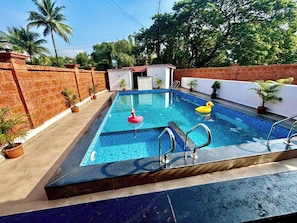 A rectangular swimming pool with a tiled edge, surrounded by a brick wall and potted plants.