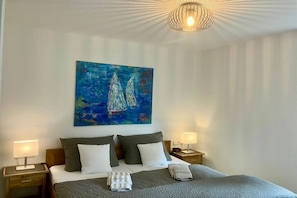 Una habitación de hotel con una cama, dos mesitas de noche, un cuadro en la pared y una lámpara en el techo.