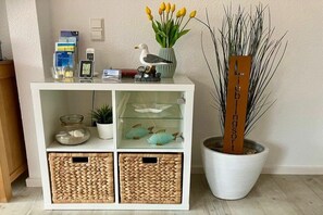 A white console table with storage baskets, a vase with yellow tulips, a wooden sign, and decorative items including a seagull figurine and fish-shaped objects. - Möwensteert in the house Meeresgruß (Juist)