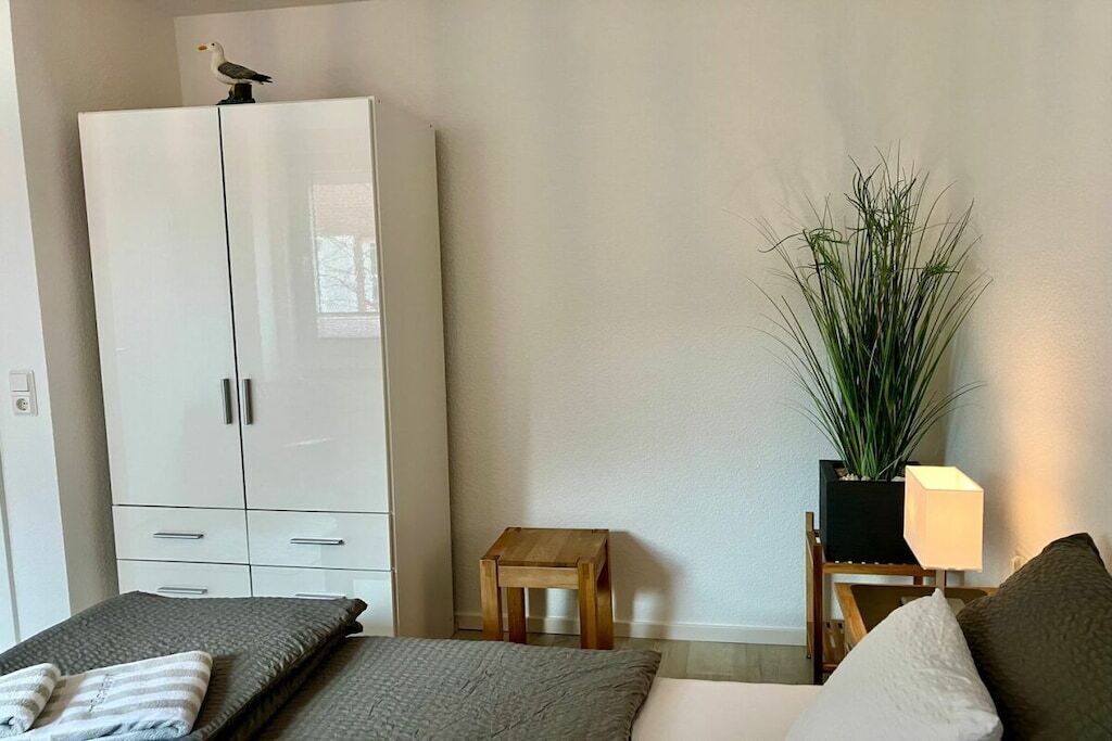 A bedroom with a bed, a wardrobe, a small table, a lamp, and a potted plant.
