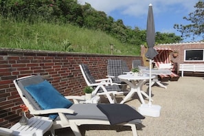 Un patio con sillones blancos y una mesa, un muro de ladrillo y un edificio pequeño al fondo.