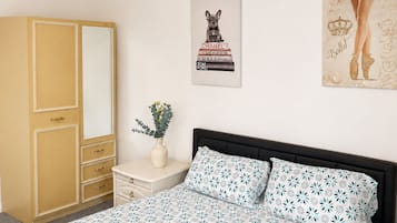 Ein Schlafzimmer mit Bett, Kleiderschrank, Nachttisch, einer Vase mit Blumen und zwei Wandbildern.