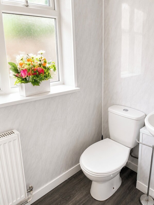 Ett badrum med en toalett, ett vitt element och ett fönster med en blomsteruppsättning.