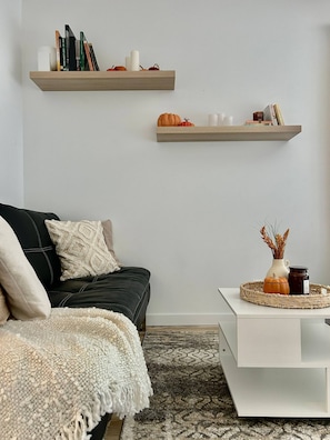 A modern living room with a black sofa, white throw blanket, and a white coffee table with decorative items.