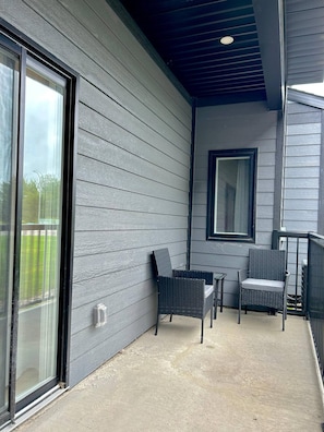 A covered porch with two wicker chairs and a small table, a sliding glass door, and a window.