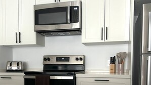 Eine moderne Küche mit weißen Schränken, einer Edelstahl-Mikrowelle, einem Toaster, einem Backofen und einem Kühlschrank.