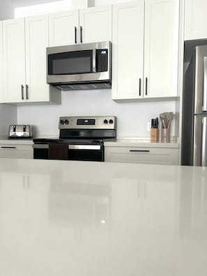 A modern kitchen with white cabinets, a stainless steel microwave, a toaster, an oven, and a refrigerator.