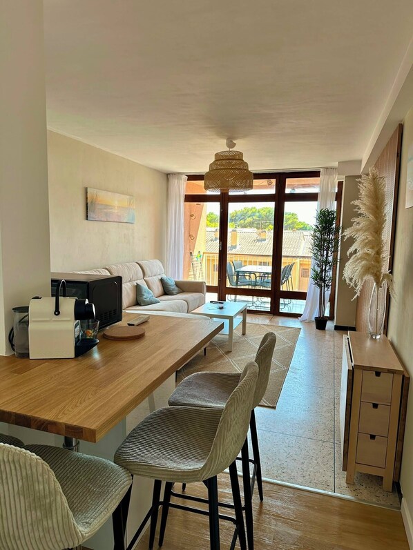 Een moderne woonruimte met een houten eettafel, een bank en een televisie. Er is een balkon met uitzicht op de stad.