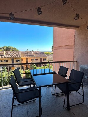 Een balkon met een tafel en stoelen, met uitzicht op een woonwijk met pannendaken.