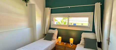 A twin room with two beds, a window with curtains, bedside lamps, and a small plant on the wall.